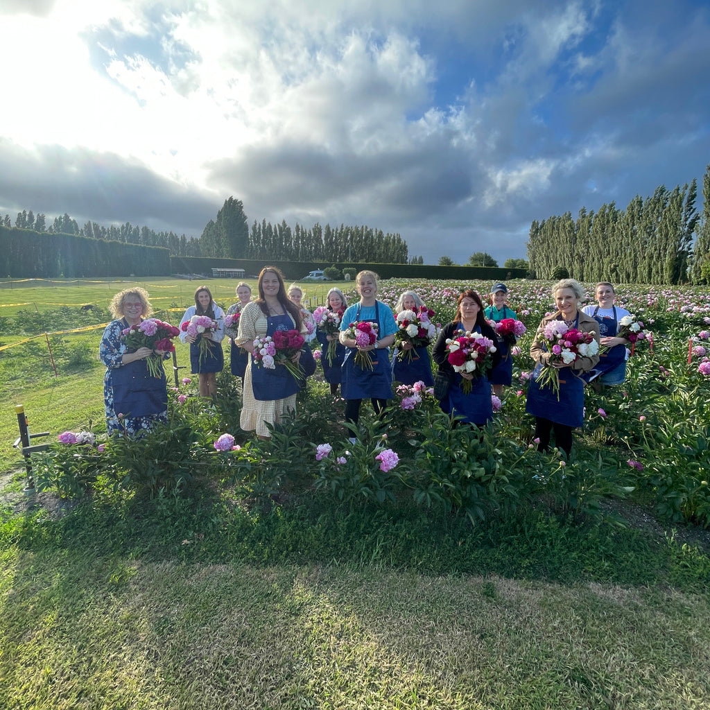 Group of people standing in a field with peonies and blue sky.