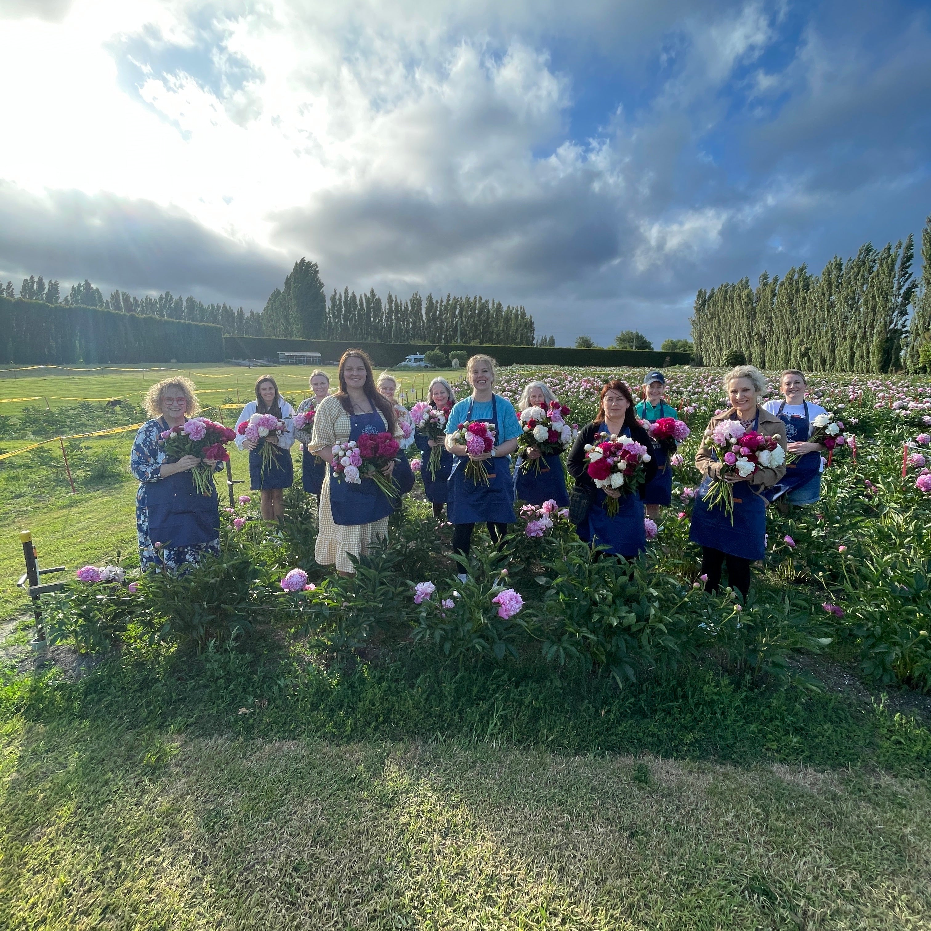 Group of people standing in a field with peonies and blue sky.