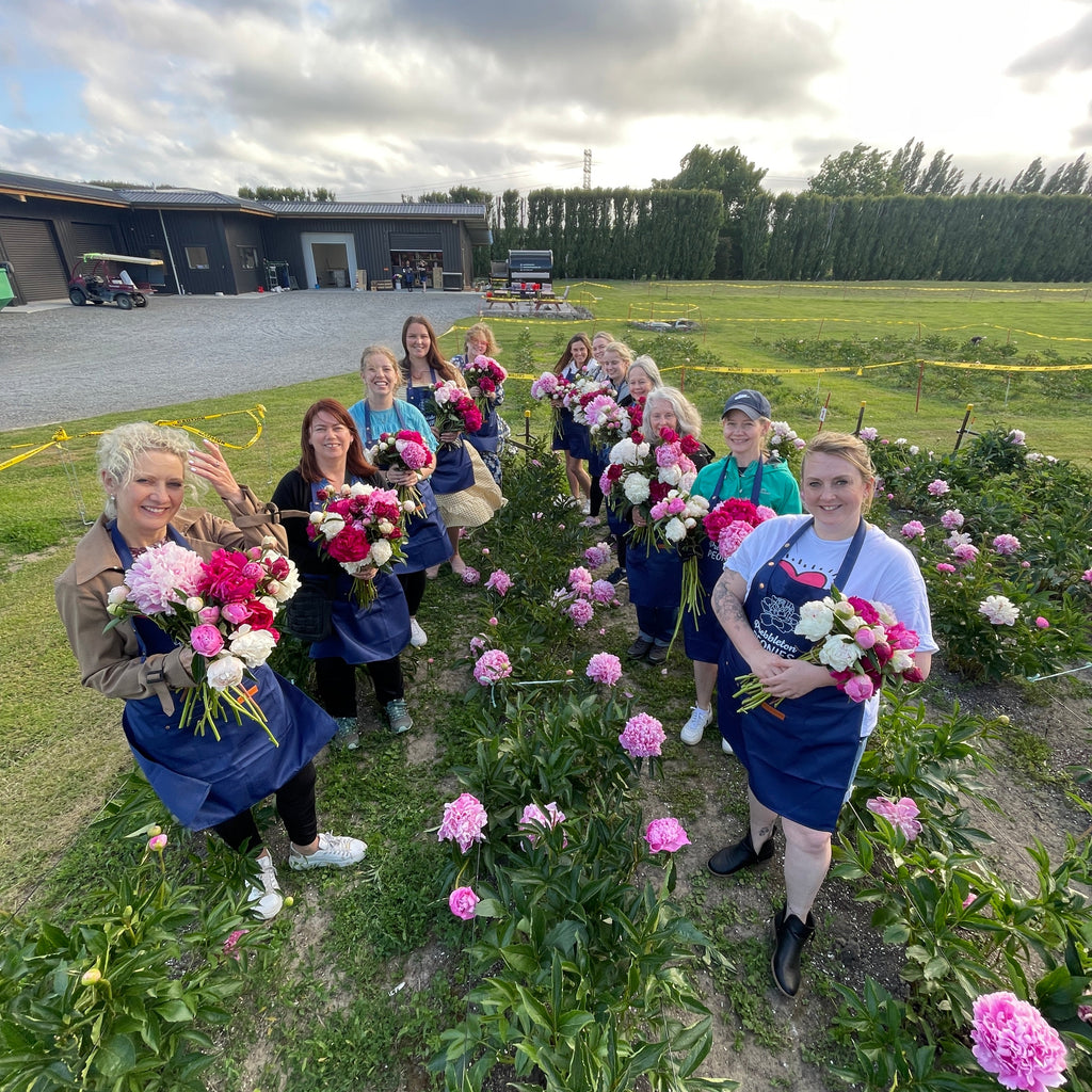 Group of people with floral peony arrangements standing in a field on a sunny day.