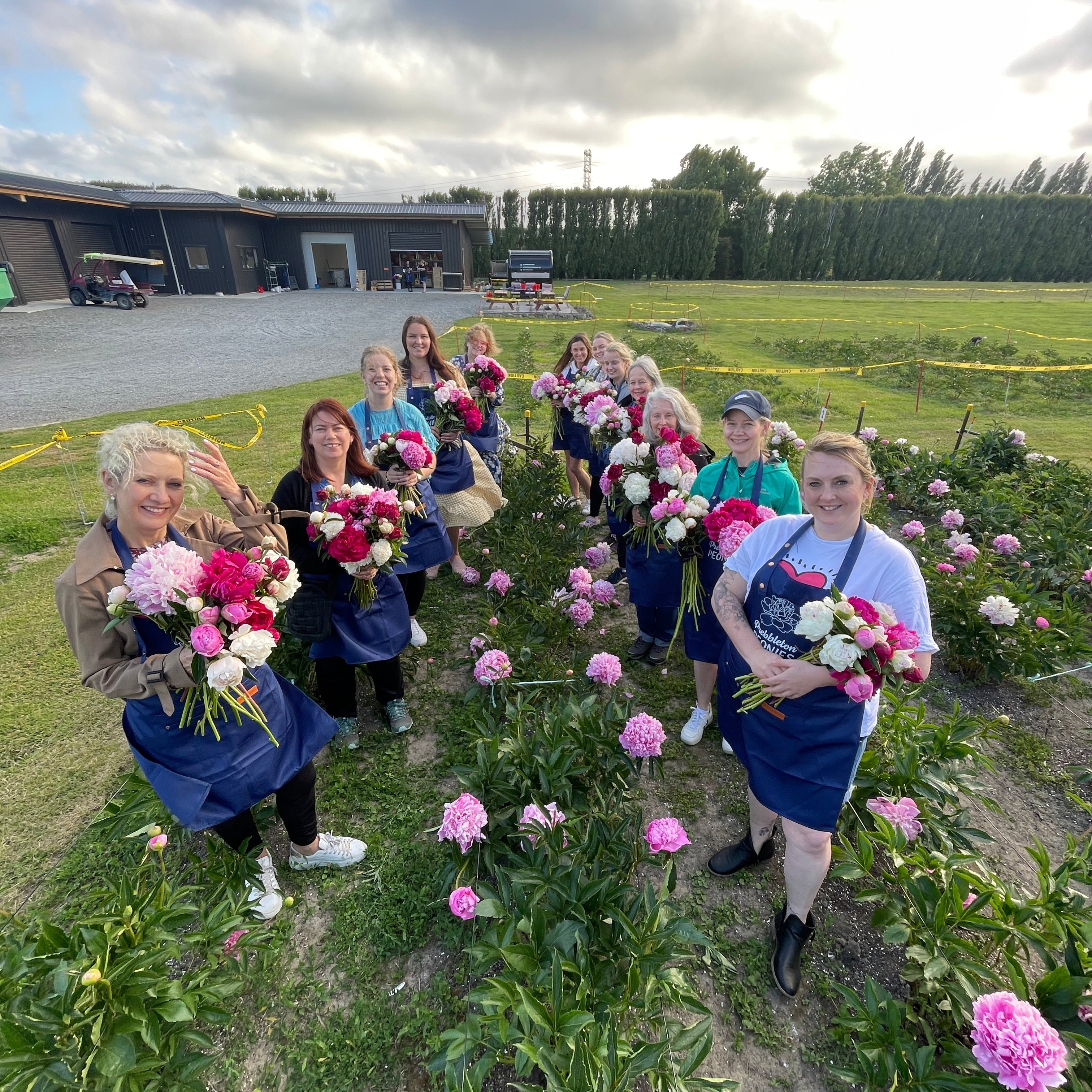 Group of people with floral peony arrangements standing in a field on a sunny day.
