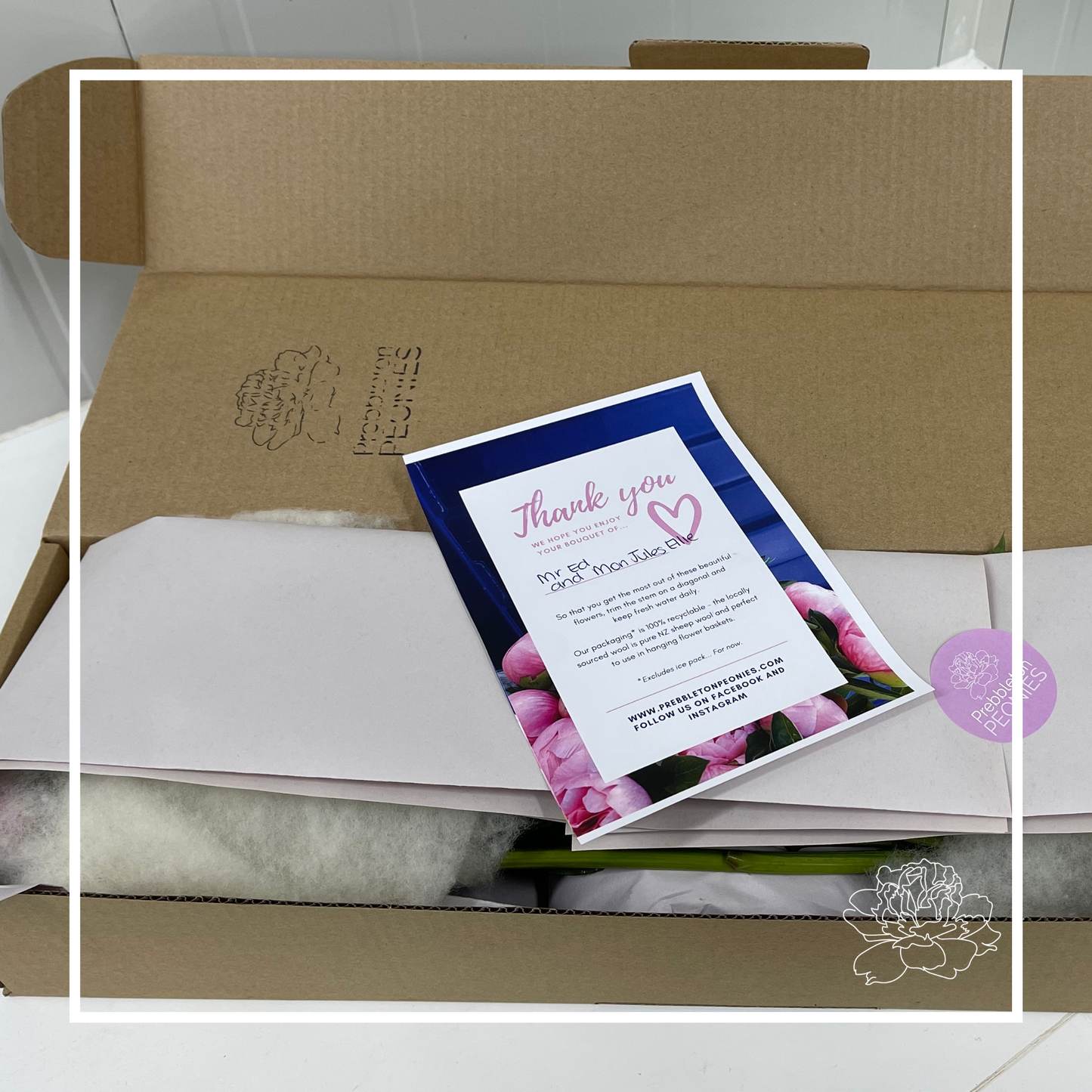 half packaged delivery box for peonies. An A4 flyer lays over the top of the packaging to show a hand written note. the brown box shows hints of the flowers inside along with wool and paper packaging to protect the flower. a black logo is stamped on the top of the box. The image is framed in a white box graphic with the prebbleton peonies logo on the bottom right corner. 
